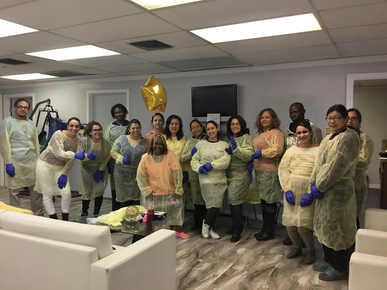A nurse aide class at Stone Academy standing together in disposable gowns and gloves after a skills session